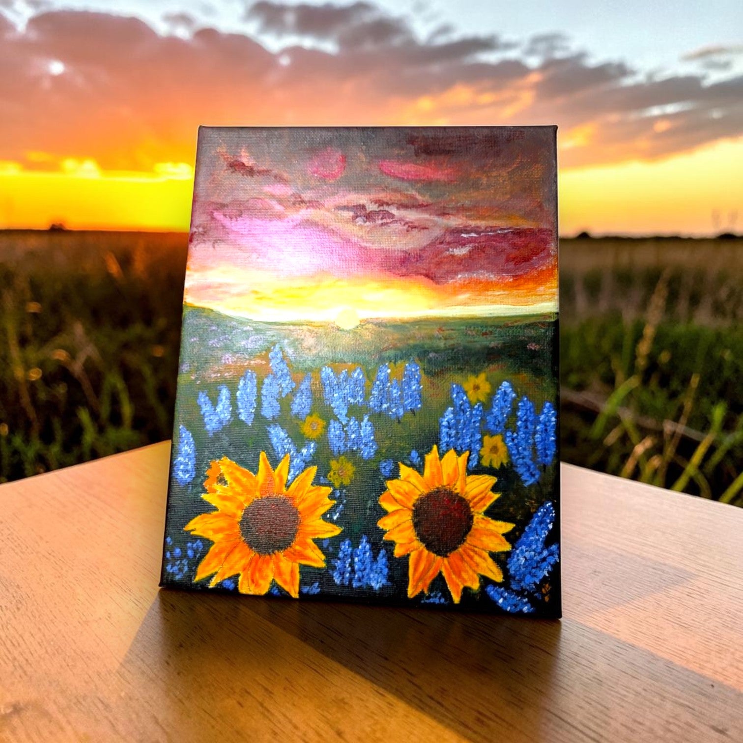 Canvas painting of sunflowers and bluebonnets with a sunset landscape in the background.