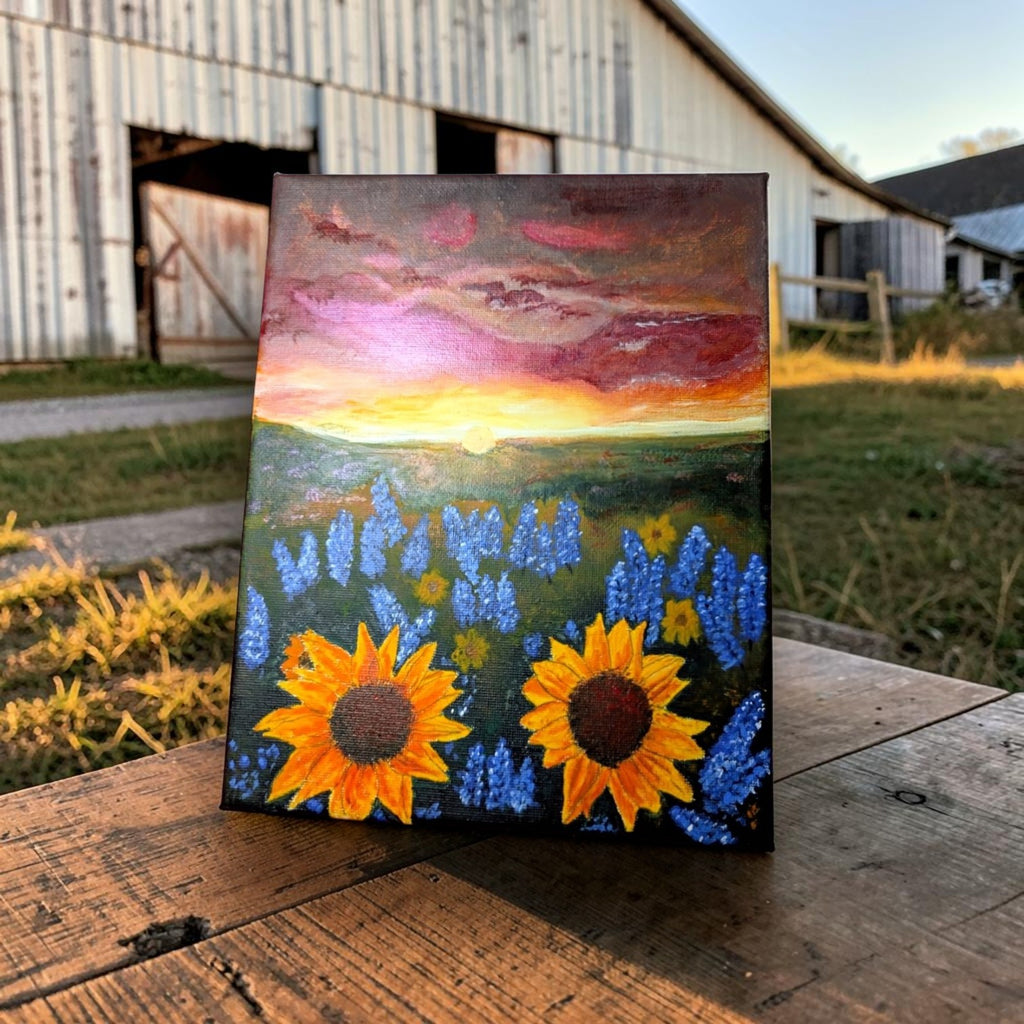Hand-painted acrylic landscape of vibrant yellow sunflowers and purple bluebonnets in a field under a dramatic Texas sunset with shades of orange and pink.